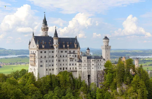 Neuschwanstein Şatosu, Almanya 'nın Bavyera şehrinde bulutlu mavi bir gökyüzünün altında ormanla çevrili bir tepeye tünemişti..