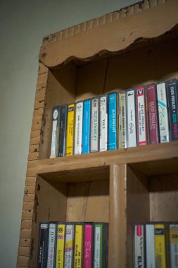 Yıpranmış ve kirli bir duvara asılı klasik tip ahşap bir duvar rafının ayrıntıları. Rafta eski kasetler var, pencerenin yanında düzgünce ve estetik olarak düzenlenmiş..