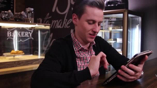 Sonriente hombre escribiendo texto en una tableta PC en la cafetería — Vídeos de Stock