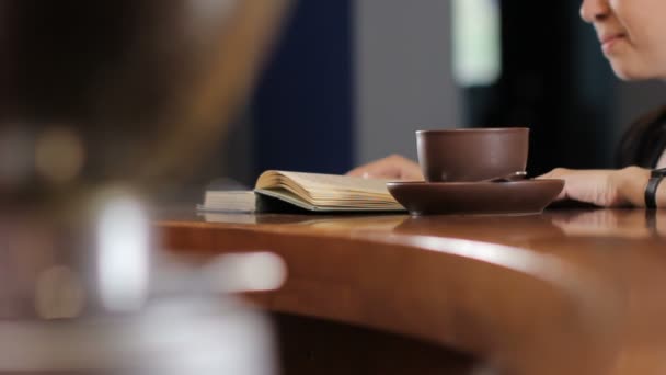 Young woman is reading a book, drinking coffee and smile. Medium shot. Background — Stock Video