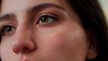 Kız sakince ve dikkatle bir şeyi inceliyor. Gözlere yakın çekim. Kahverengi gözlü. Yan yana görünüm