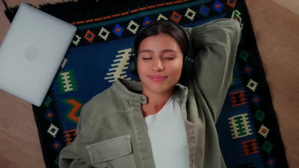 Egy fiatal lány fekszik a padlón fülhallgatóban, és mosollyal az arcán zenét hallgat. — Stock videók