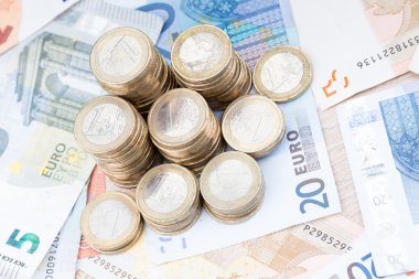 Pile of coins on a layer of bank notes diagonal