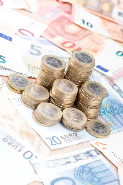 Pile of coins on a layer of bank notes vertical