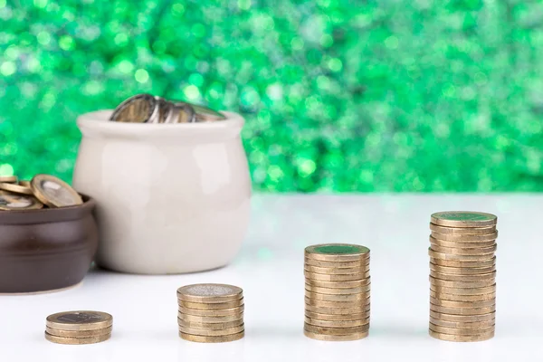 Stacks of coins showing an increase on a green lighted background with two pots full of coins