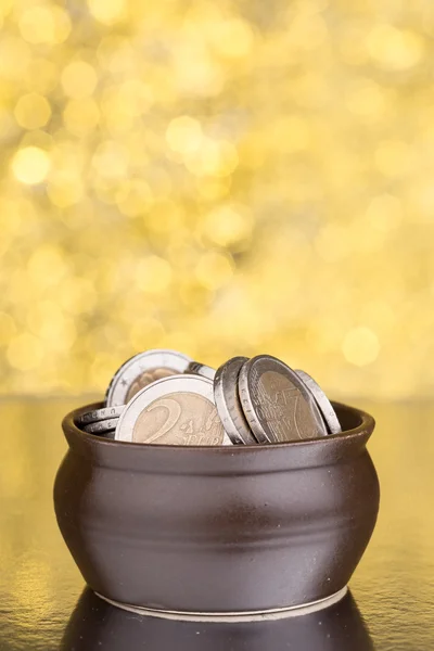 Brown pot full of coins on golden blurry background