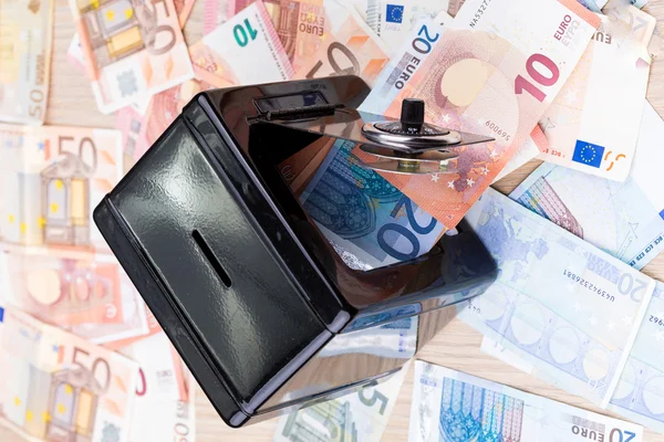 Black metal coin bank with bank notes on a desk