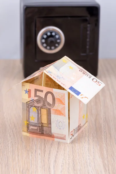 Bank note house with black coin bank on desk - real estate, home savings, mortgage, rent concept
