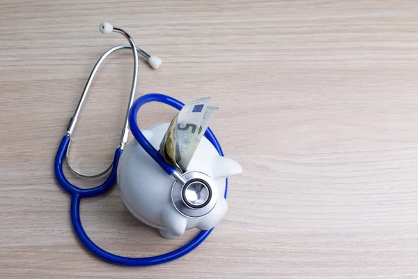 Piggy bank with a stethoscope on a wooden desk - medical costs concept