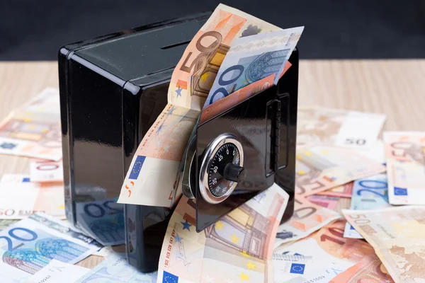 Black metal coin bank with bank notes on a desk