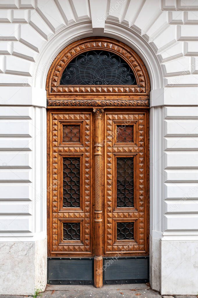 Details of European style classic old-fashion elegant wood carving door panels made of wood and decorated with wrought iron at a white concrete building in Rome, Italy