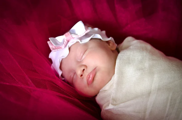 Dormir niña recién nacida en un cabestrillo con un arco —  Fotos de Stock