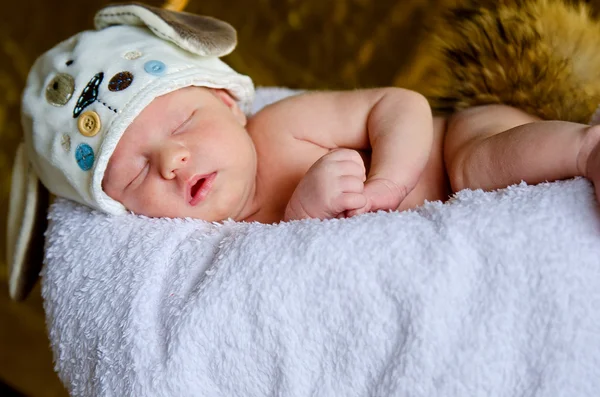 Beyaz ekose kulaklara ile şapkalı bir yeni doğmuş bebek uyur — Stok fotoğraf