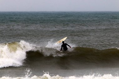 Kuzey İsrail 'deki Akdeniz' de yüksek dalgalarda sörf yapmak. Özel bir sörf tahtasında büyük bir deniz dalgasının tepesinde süzülüyordu.. 