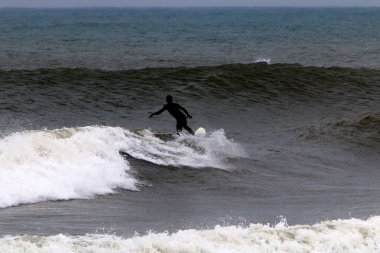 Kuzey İsrail 'deki Akdeniz' de yüksek dalgalarda sörf yapmak. Özel bir sörf tahtasında büyük bir deniz dalgasının tepesinde süzülüyordu.. 