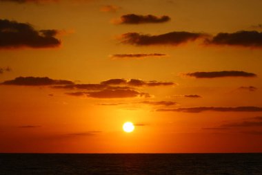 Güneş ufukta gökyüzünün alevli kırmızı ışığına karşı batar. 