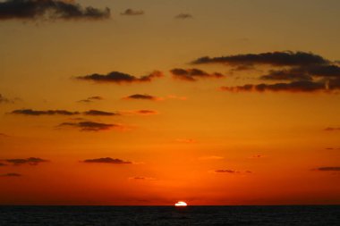 Güneş ufukta gökyüzünün alevli kırmızı ışığına karşı batar. 