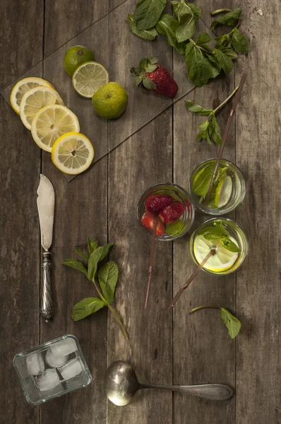 Cócteles con fresa, lima y limón y hielo sobre una vieja mesa de madera — Foto de Stock
