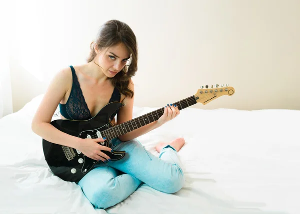 Sexy meisje in zwarte lingerie zittend op een bed met gitaar — Stockfoto