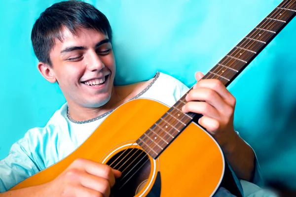 Hombre riendo con una guitarra amarilla en sus manos sobre fondo turquesa —  Fotos de Stock