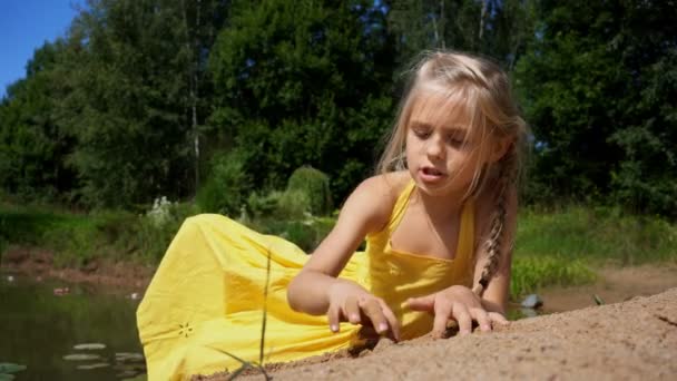 Beautiful girl in yellow sundress sitting by the pond with water lilies — Stock Video