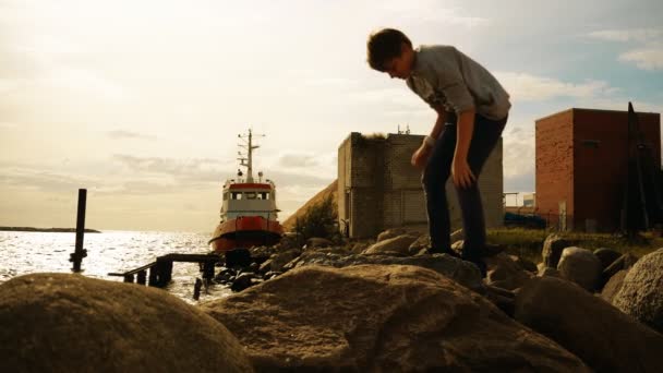 Jongen in de haven aan zee naast een oude boot — Stockvideo