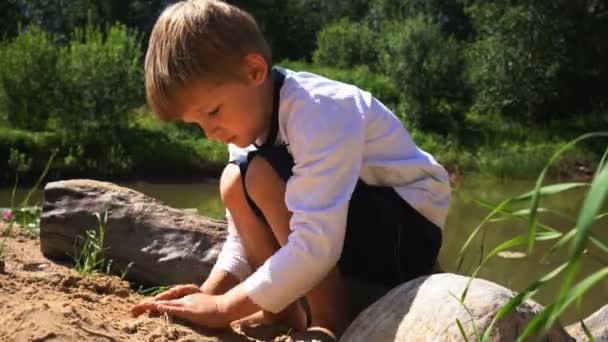 Piccolo ragazzo si siede in un tronco sulla riva di uno stagno — Video Stock