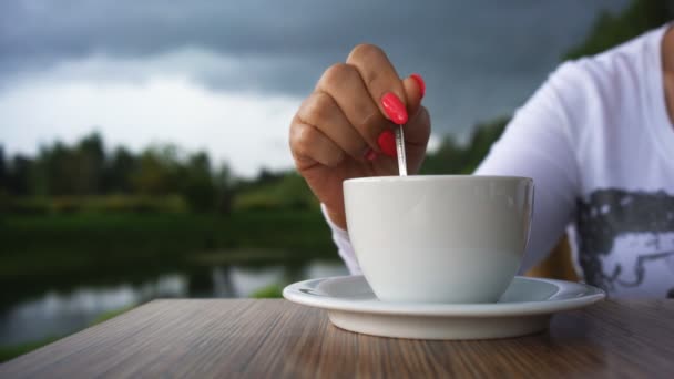 Womans hand with red nail polish and a cup of coffee on the background of beautiful scenery. — Stock Video