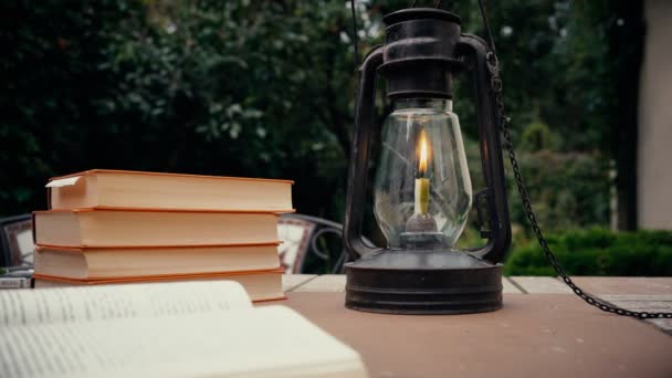 Lâmpada de querosene e stapka livros antigos sobre a mesa no jardim. mão coloca o livro sobre a mesa. Outono — Vídeo de Stock