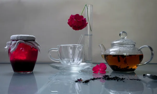 Τρόπος ζωής. Τράπεζα της μαρμελάδα βατόμουρο με τσάι και pelargonium λουλούδι σε ένα γυάλινο τραπέζι. — Φωτογραφία Αρχείου