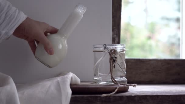 Naturaleza muerta rústica. mano femenina está vertiendo la leche de una botella en un frasco de vidrio — Vídeos de Stock
