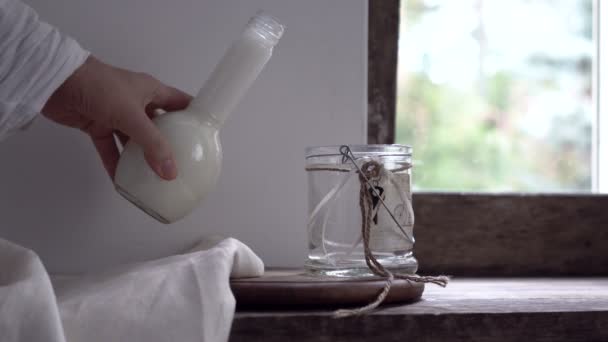 Rustic still life. female hand is pouring milk from a bottle into a glass jar — Stock Video