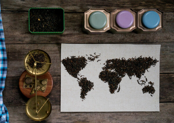 map of the world, lined with tea leaves on old paper. vintage. green tea, a towel, scales, weights on rustic wooden table. top view. flat lay