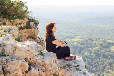 woman in a black tracksuit sitting on the cliff and meditates clipart