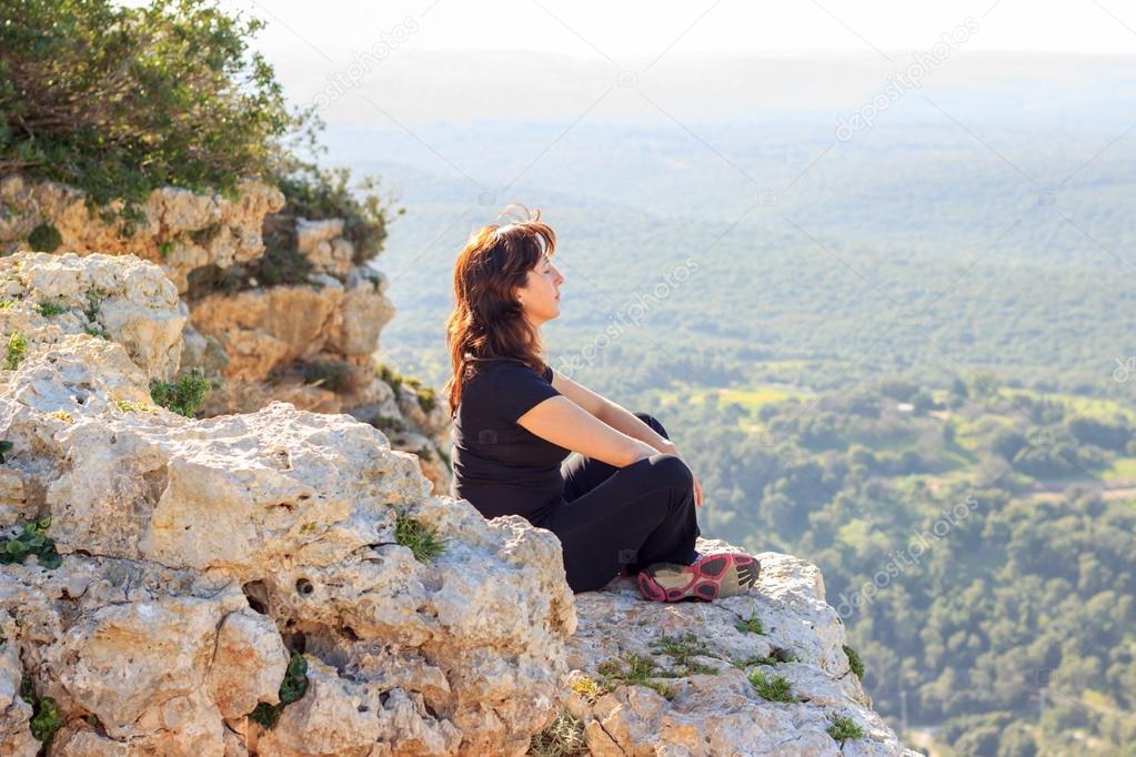woman in a black tracksuit sitting on the cliff and meditates