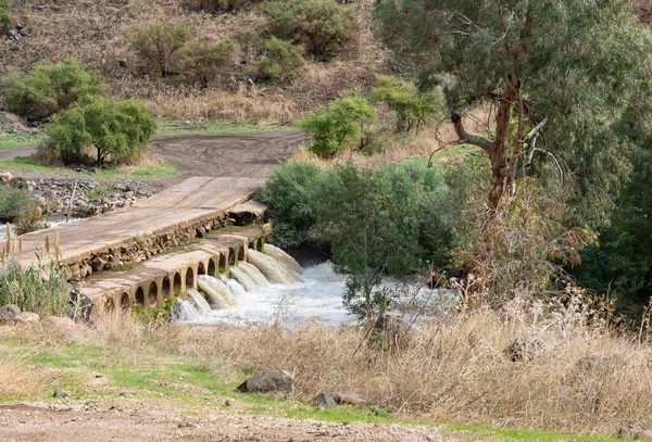 A country road passes through a concrete bridge with pipes for water passage over the Jordan River in the Golan Heights in northern Israel — Stock Image Country Road Passes Concrete Bridge Pipes Water Passage Jordan River Royalty Free Stock Images