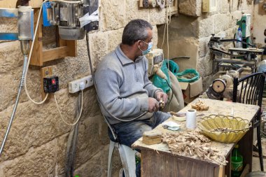 Beytüllahim, İsrail, 09 Aralık 2020: Bir işçi oturuyor ve İsrail 'in Beytüllahim kentindeki bir hediyelik eşya dükkanında zeytin ağacından hediyelik eşya yapıyor.