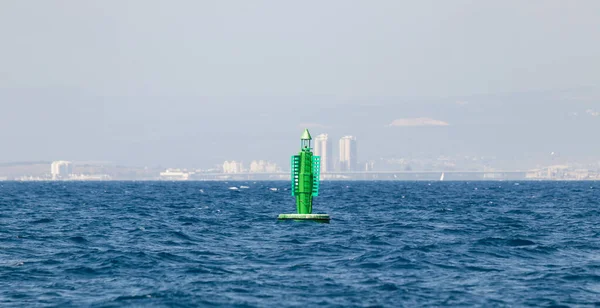 A fencing light beacon buoy is located in the water area of the Haifa Bay, against the background of Haifa city, in the Mediterranean Sea, near the port of Haifa in Israel
