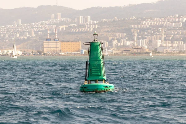 A fencing light beacon buoy is located in the water area of the Haifa Bay, against the background of Haifa city, in the Mediterranean Sea, near the port of Haifa in Israel