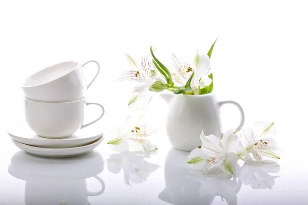 Graceful white flowers and coffee set on a glossy background. Alstrameria, two cups and a milk jug. Still life