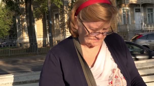 Babcia zmarszczki na twarzy i okulary uważnie czytać książki, siedząc na ławce — Wideo stockowe