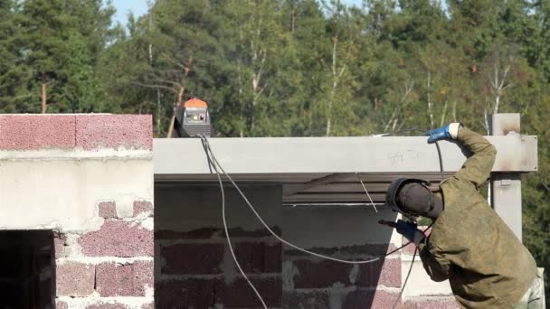 Özel giysili merdiven aşçılar elektrot kaynak makine kirişler ve kanal çubukları yeni bir ev üzerinde duran genç bir adam — Stok video