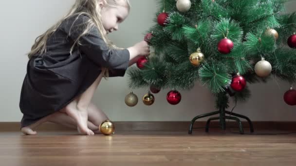 Bambina delicatamente appendere ghirlanda rossa e oro sul abete rosso verde — Video Stock