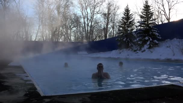 Um jovem vem para a terra depois de nadar na piscina nas águas termais no frio dia de neve de inverno — Vídeo de Stock