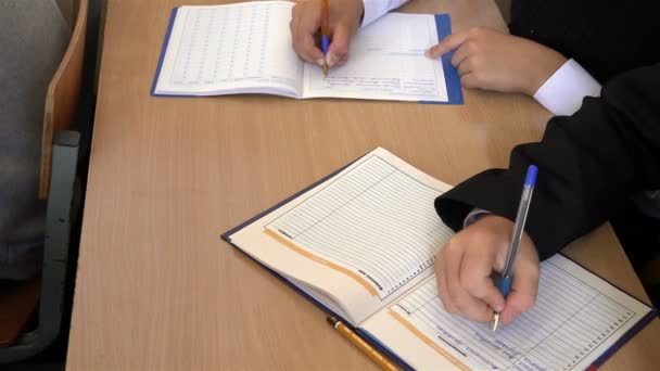 Eleverna sitter vid ett skrivbord skrivuppgift från en lärare i en dagbok — Stockvideo