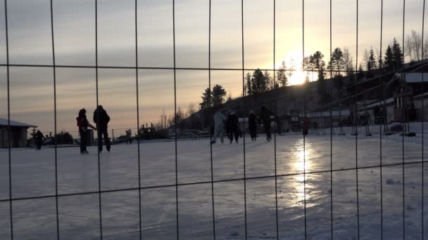 ロシア、レニングラード地域トゥタリ公園、1月2、2016:日没時に冬の太陽の光線の中で開かれたフェンスのリンクでスケート — ストック動画