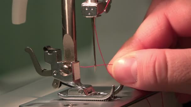 Женская рука кладет красную шелковую нить в иглу швейной машинки — стоковое видео