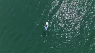 Sörf tahtasındaki bir kız suyun parlak yüzeyinde yüzer.