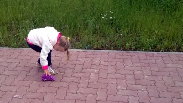 A kislány egy játékautó gördülő a járdán — Stock videók