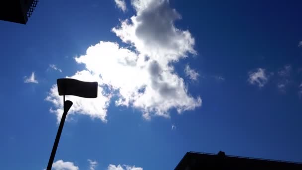 Witte wolken drijven over de architectuur van de stad door een straat lamp — Stockvideo